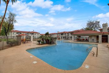 A large swimming pool surrounded by a fence and palm trees. at San Montego Apartments, Mesa, AZ